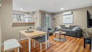 A modern living room with a grey sofa, a small round coffee table, and a dining area with a wooden table and chairs.