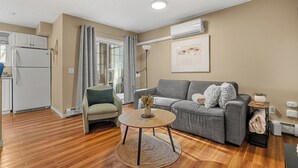 Un salon moderne avec un canapé gris, une table basse ronde et un coin cuisine doté d’un réfrigérateur blanc.
