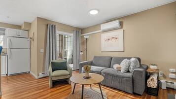 Ein modernes Wohnzimmer mit einem grauen Sofa, einem runden Couchtisch und einer Küchenzeile mit einem weißen Kühlschrank.