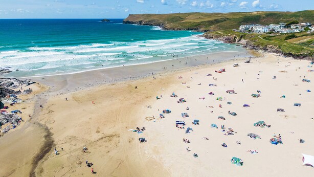 A beach with people, umbrellas, and a coastal town in the background. - Baywatch Sands (Wadebridge)