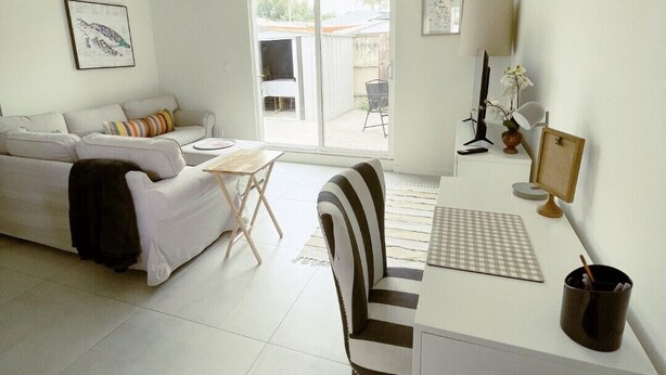 A spacious living room with a white sofa, a striped chair, a small table, and a desk with a lamp. - Sunshine on Sylvan! (Los Angeles)