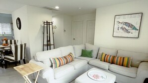 A modern living room with a white sofa, striped pillows, a wooden side table, and a framed artwork on the wall. - Sunshine on Sylvan! (Los Angeles)