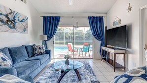A living room with a blue sofa, a glass coffee table, and a TV on a stand.