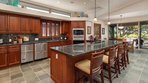 A spacious kitchen with wooden cabinets, stainless steel appliances, and a large island with bar stools. - Mauna Lani Villages luxurious Villa with Private Beach Access! (Waimea)