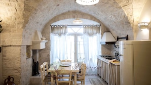 Une cuisine rustique aux murs en pierre, une table à manger avec des chaises et un luminaire suspendu.