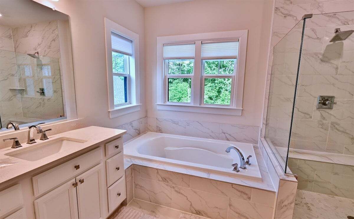 Un baño con una bañera grande, dos lavamanos, ducha y ventana con vistas a la vegetación.