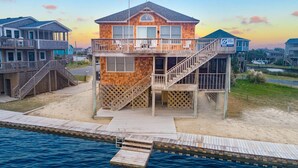 A beachfront house with a wooden deck, a staircase leading to a balcony, and a view of the ocean. - Soundfront Dog Friendly w/ Hot Tub, Dock, Private Windsurfing Access, Foosball (Avon)