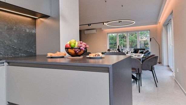 Una cocina moderna con una isla central, zona de comedor con sillas y un amplio ventanal que proporciona luz natural.