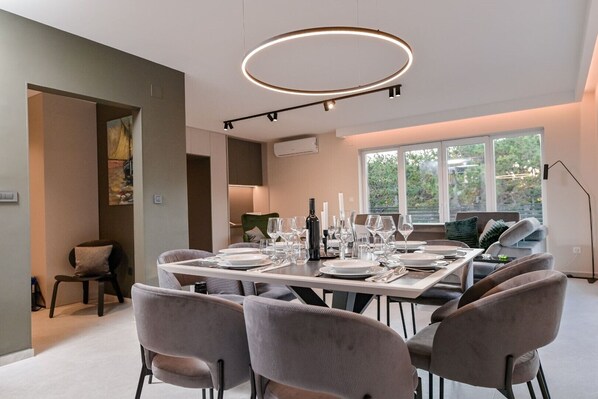 Un comedor moderno con una mesa rectangular dispuesta para seis personas, rodeada por seis sillas grises tapizadas. Una lámpara de techo circular ilumina el ambiente.
