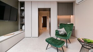 Una sala de estar moderna con un sofá de terciopelo verde, una mesita con tulipanes y un televisor de pantalla plana montado en la pared.