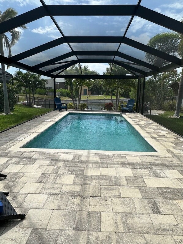 A rectangular pool with a glass enclosure, surrounded by a paved patio with a checkered pattern.