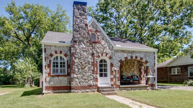 A stone house with a chimney, arched windows, and a front porch with outdoor seating. - Little Stone House in the Heart of Murfreesboro (Murfreesboro)
