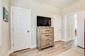 Un pasillo con puertas blancas, un aparador de madera con cajones y un televisor encima.