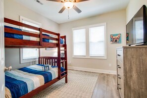 Un dormitorio con literas, ventilador de techo, televisión y cómoda.