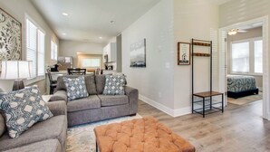 A spacious living area with a grey sofa set, a brown ottoman, and a dining table with chairs. A kitchen is visible in the background, and there is a small seating area with a patterned cushion. - Little Stone House in the Heart of Murfreesboro (Murfreesboro)