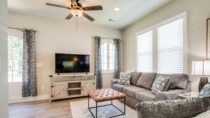 A living room with a TV, sofa, ottoman, and ceiling fan. - Little Stone House in the Heart of Murfreesboro (Murfreesboro)