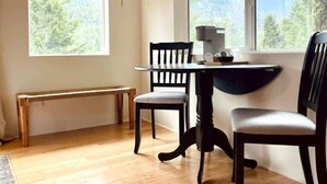 A room with a wooden bench, two chairs, a table, and a window with a view of trees and mountains. - #3 Hemlock Olympic Nat’l Park - Private Rm in Forest (Port Angeles)