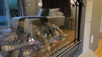 Une cheminée au décor en pierre, un lit avec une tête de lit blanche et une fenêtre donnant sur l’extérieur.