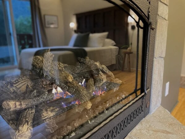 Une cheminée au décor en pierre, un lit avec une tête de lit blanche et une fenêtre donnant sur l ’extérieur.