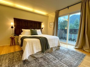 Une chambre à coucher avec un lit, des lampes de chevet, une fenêtre avec des rideaux et une vue sur la verdure à l’extérieur.