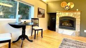 A dining area with a table and chairs, a fireplace, and a window with a view of trees. - #3 Hemlock Olympic Nat’l Park - Private Rm in Forest (Port Angeles)