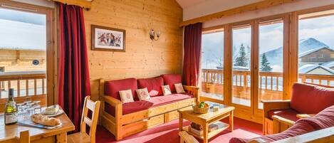 A wooden cabin interior with a sofa, dining table, and chairs.