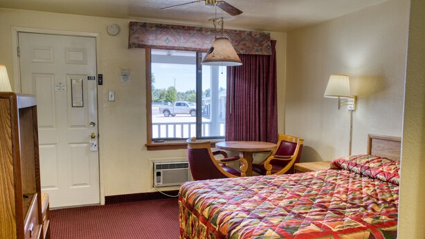 Hotelkamer met een bed, bureau, stoel, raam met gordijnen, plafondventilator en een deur.