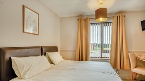 Et hotelværelse med en seng, sengegavl, et natbord med lampe, en stol og et vindue med gardiner.