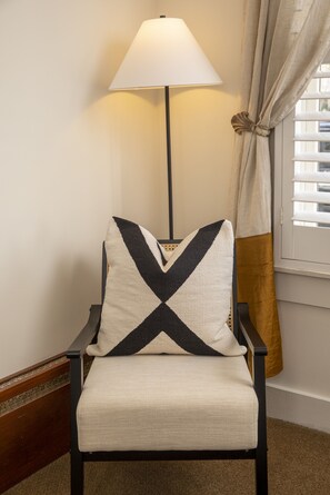 Une chaise avec un coussin aux motifs géométriques, une lampe sur pied et une fenêtre avec des stores.