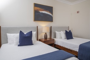 Een hotelkamer met twee bedden, een nachtkastje met een lamp en een schilderij aan de muur.
