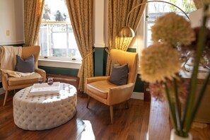 Un salon chaleureux avec un fauteuil en cuir, un pouf capitonné et un vase rempli de fleurs.