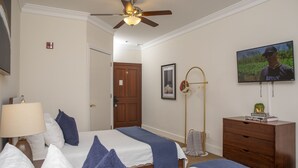 A hotel room with two beds, a ceiling fan, a TV, a wooden dresser, and a door leading to another room.