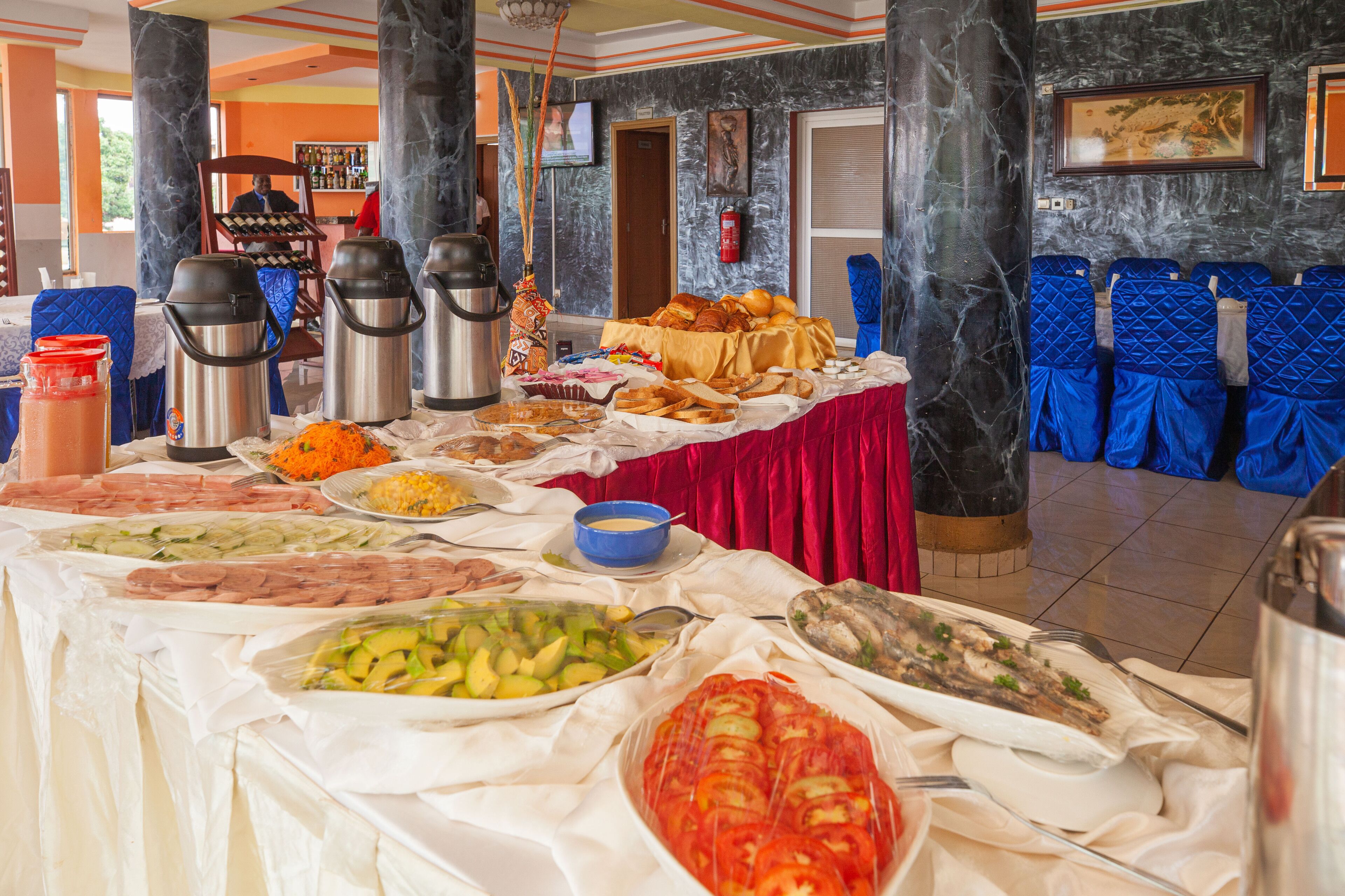 A buffet with various food items and a seating area with blue chairs.