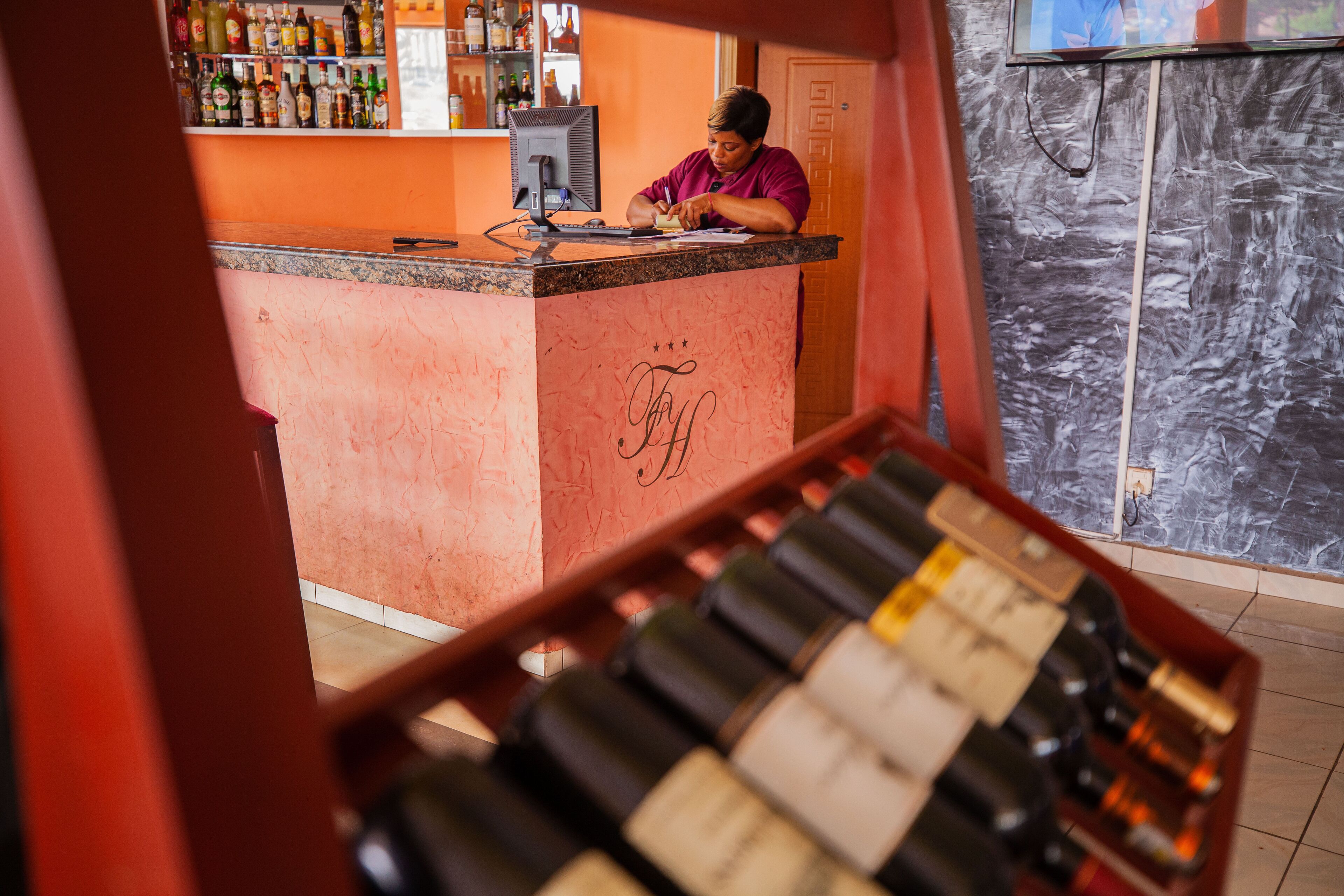A bar area with a counter, bottles of wine, and a person working behind the counter.