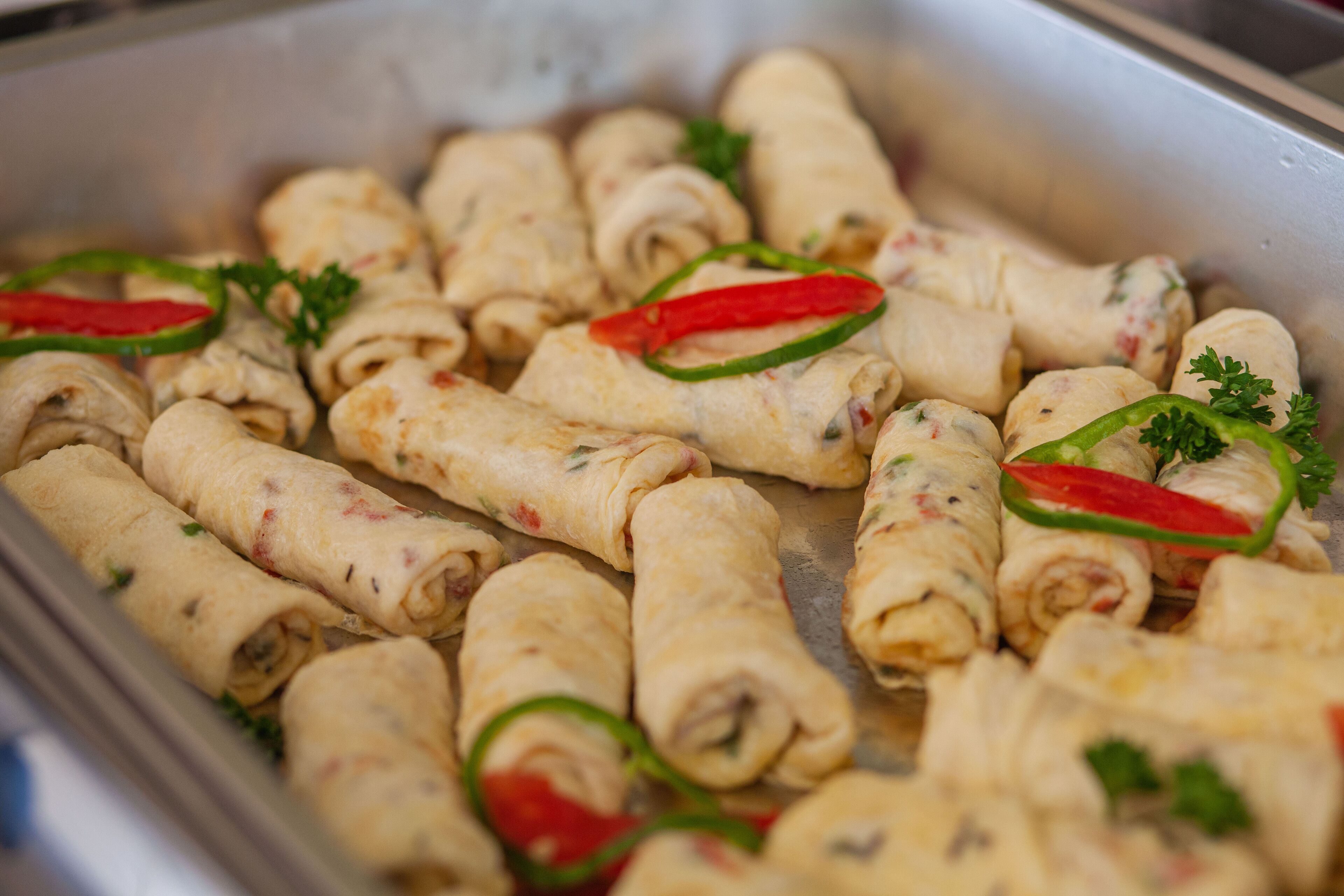 Una bandeja con rollos de comida, probablemente aperitivos, decorada con pimientos verdes y perejil.