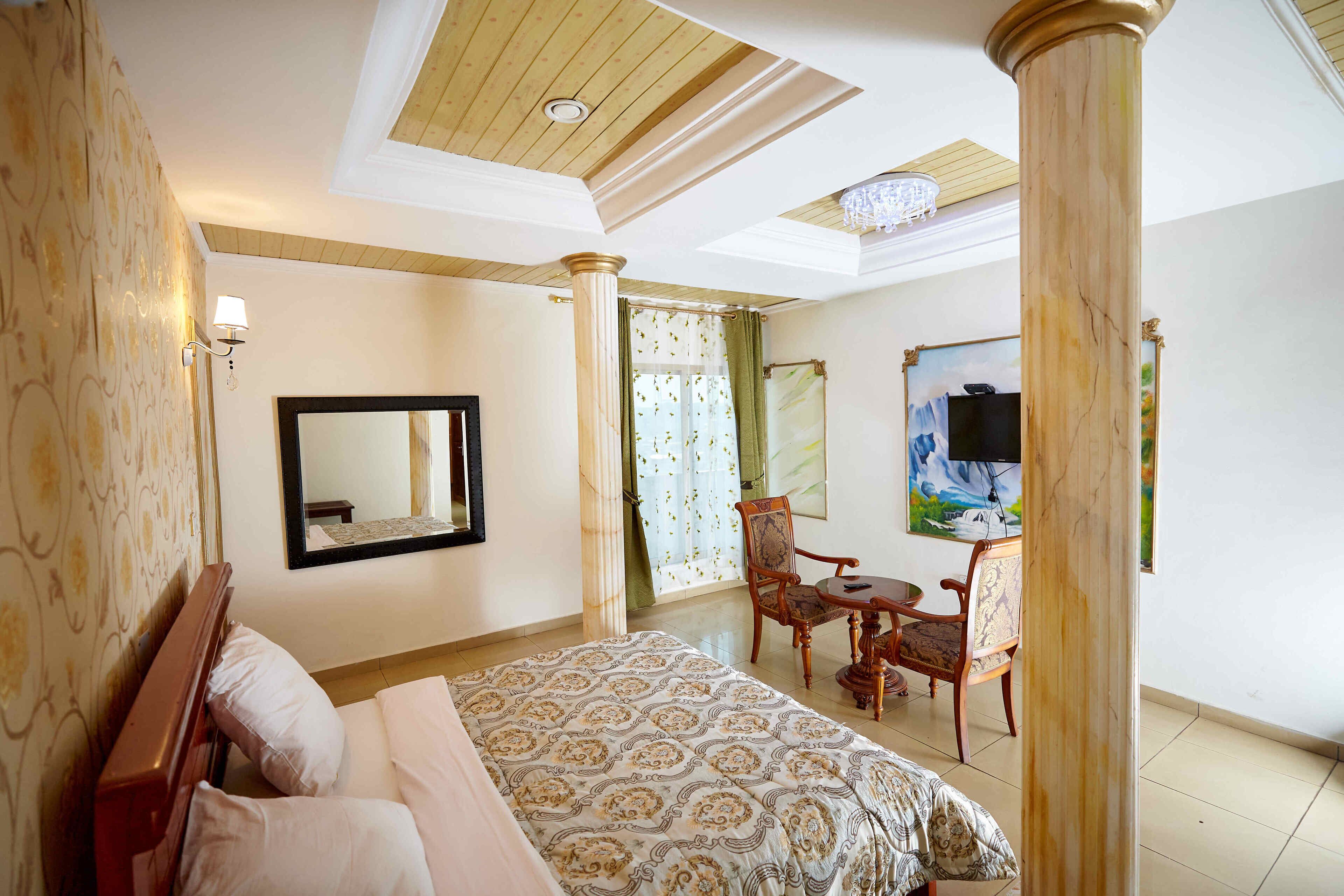 Une chambre d’hôtel avec un lit, une chaise, une table, un miroir et un tableau au mur.
