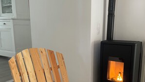 Ein Holzstuhl mit zwei Kissen, ein schwarzer Kaminofen und ein weißes Schränkchen im Hintergrund.