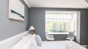 A bedroom with a large bed, a window with blinds, a chair, and a lamp.