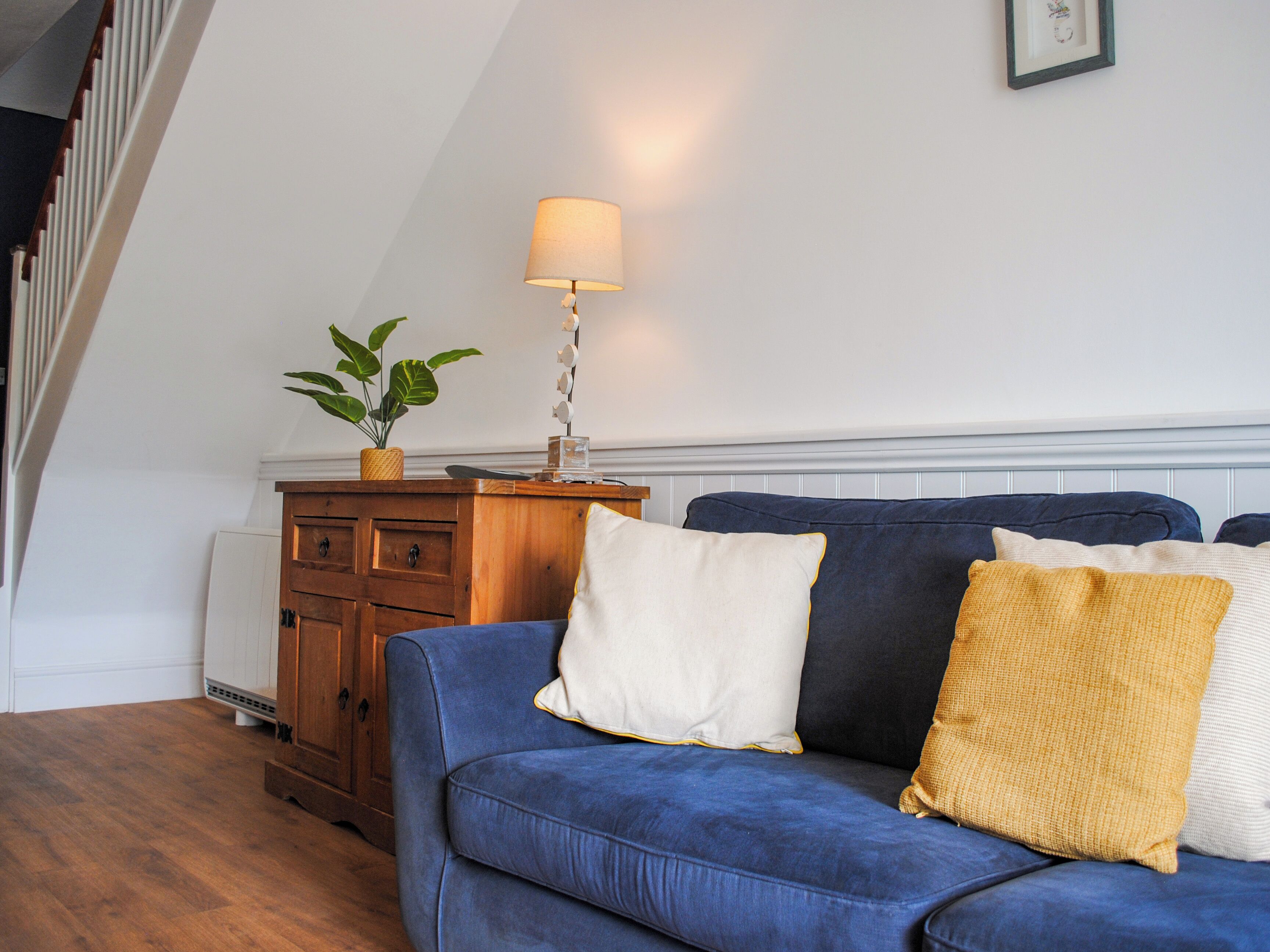 A living room with a blue sofa, a wooden cabinet, a lamp, and a potted plant.