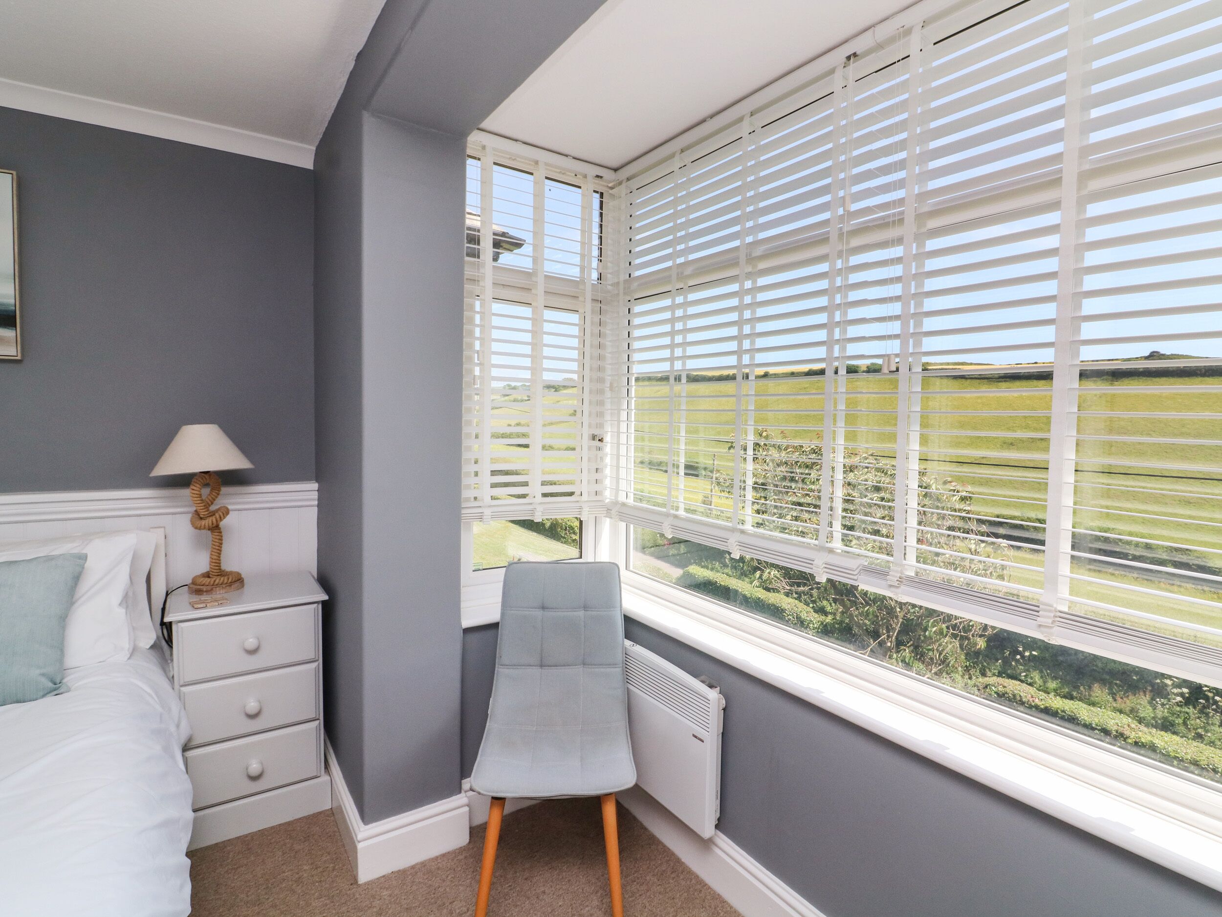 A bedroom with a bed, a chair, a nightstand, and a window with blinds.