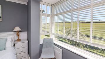 A bedroom with a bed, a chair, a nightstand, and a window with blinds.