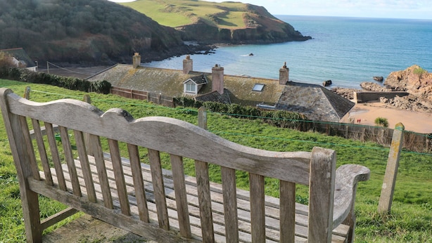 A bench overlooking a coastal village with houses and a view of the sea.