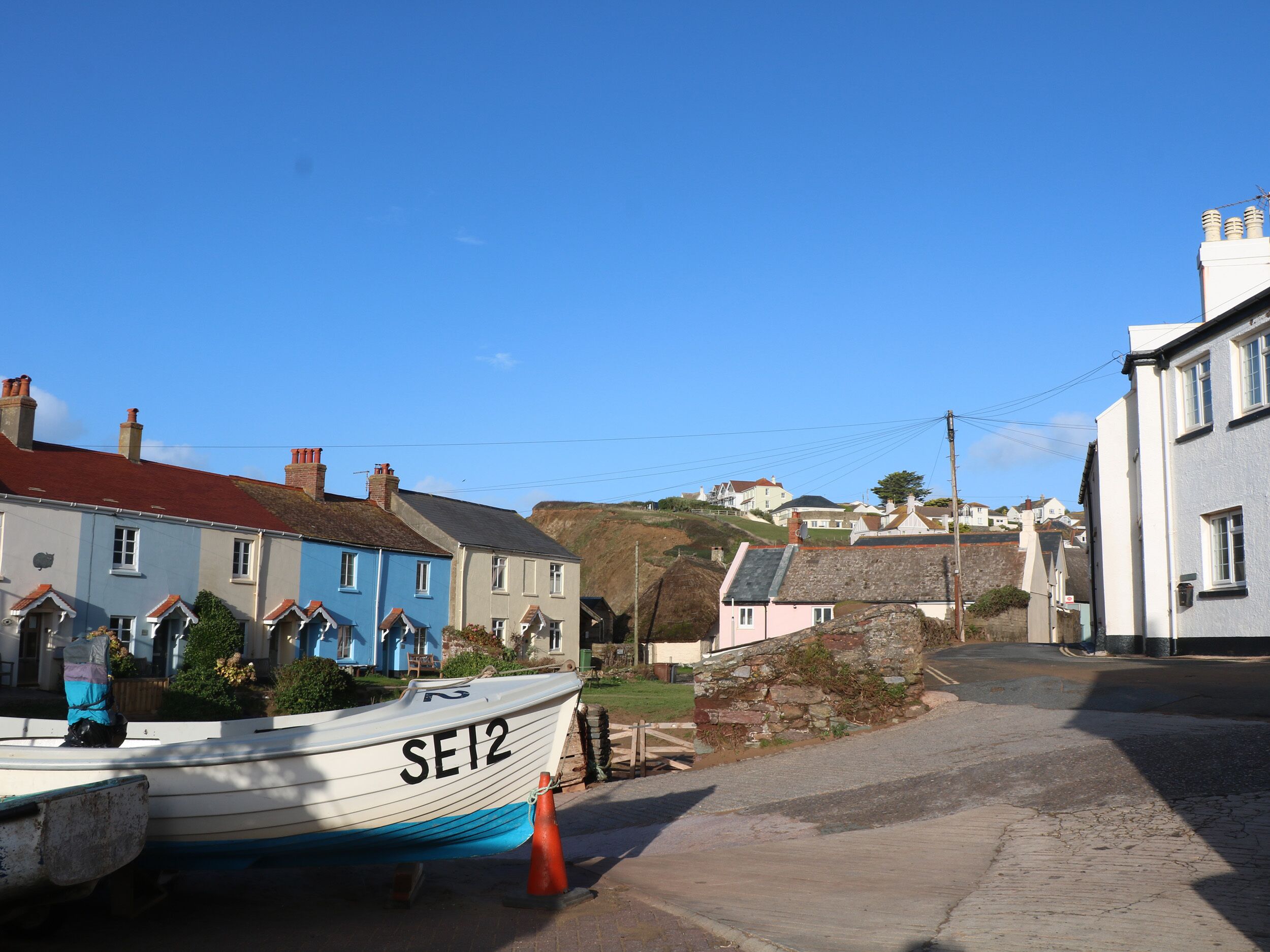 Une ville côtière bordée d’une rangée de maisons mitoyennes, un bateau portant le numéro SE12 et un mur de pierre.