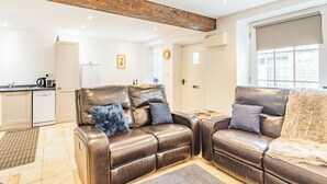 A modern living room with leather sofas, a kitchen area, and a large window. - Claro Cottage - UK37450 (Pateley Bridge, near Harrogate)