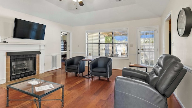 Un salon avec une cheminée, des fauteuils en cuir, une table basse en verre et un ventilateur de plafond.