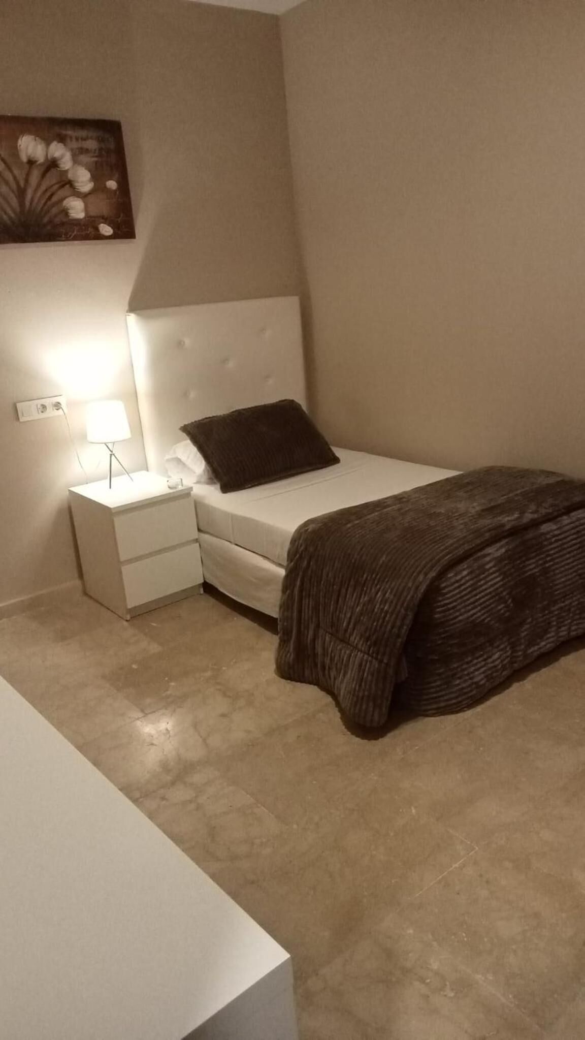 A bedroom with a bed, a nightstand, a lamp, and a painting on the wall.