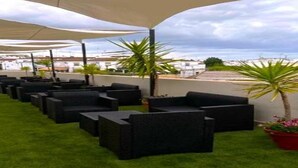 Een terras op het dak met buitenmeubels, groen en uitzicht op de stad.