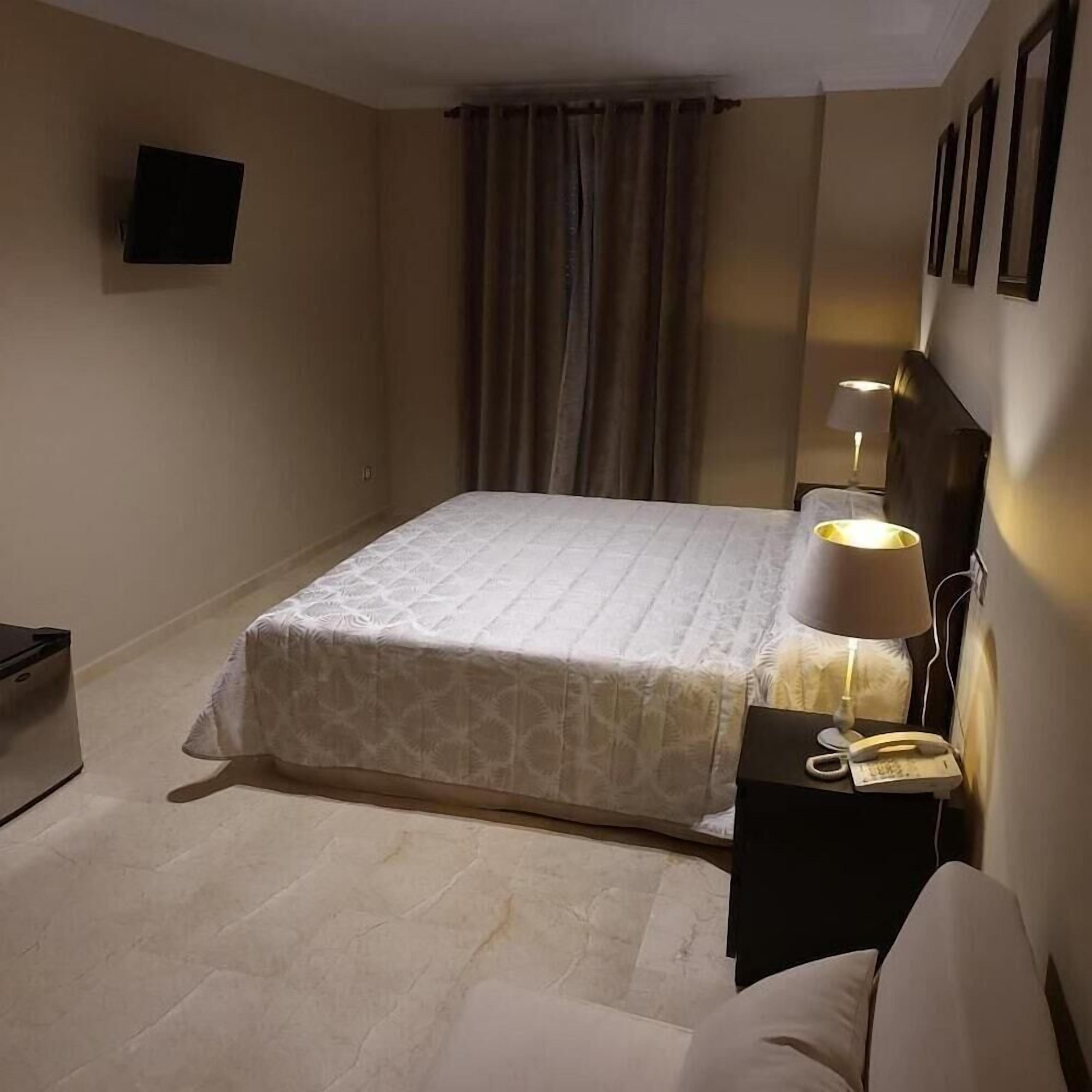 Une chambre d’hôtel avec un lit, une lampe de chevet, un téléphone et un téléviseur fixé au mur.
