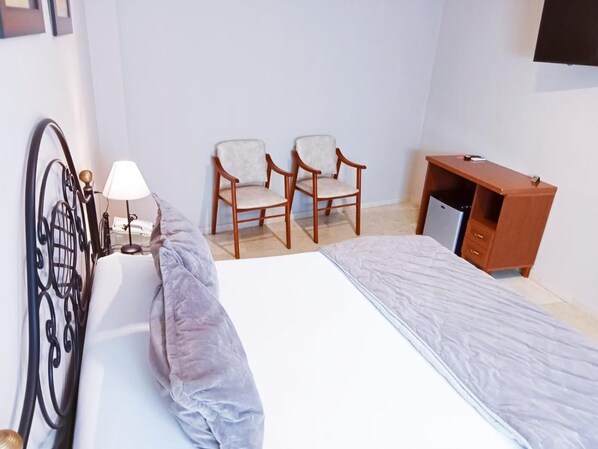 A bedroom with a bed, two chairs, a desk, and a lamp. - Hotel Sol Sanlucar (Sanlucar la Mayor)