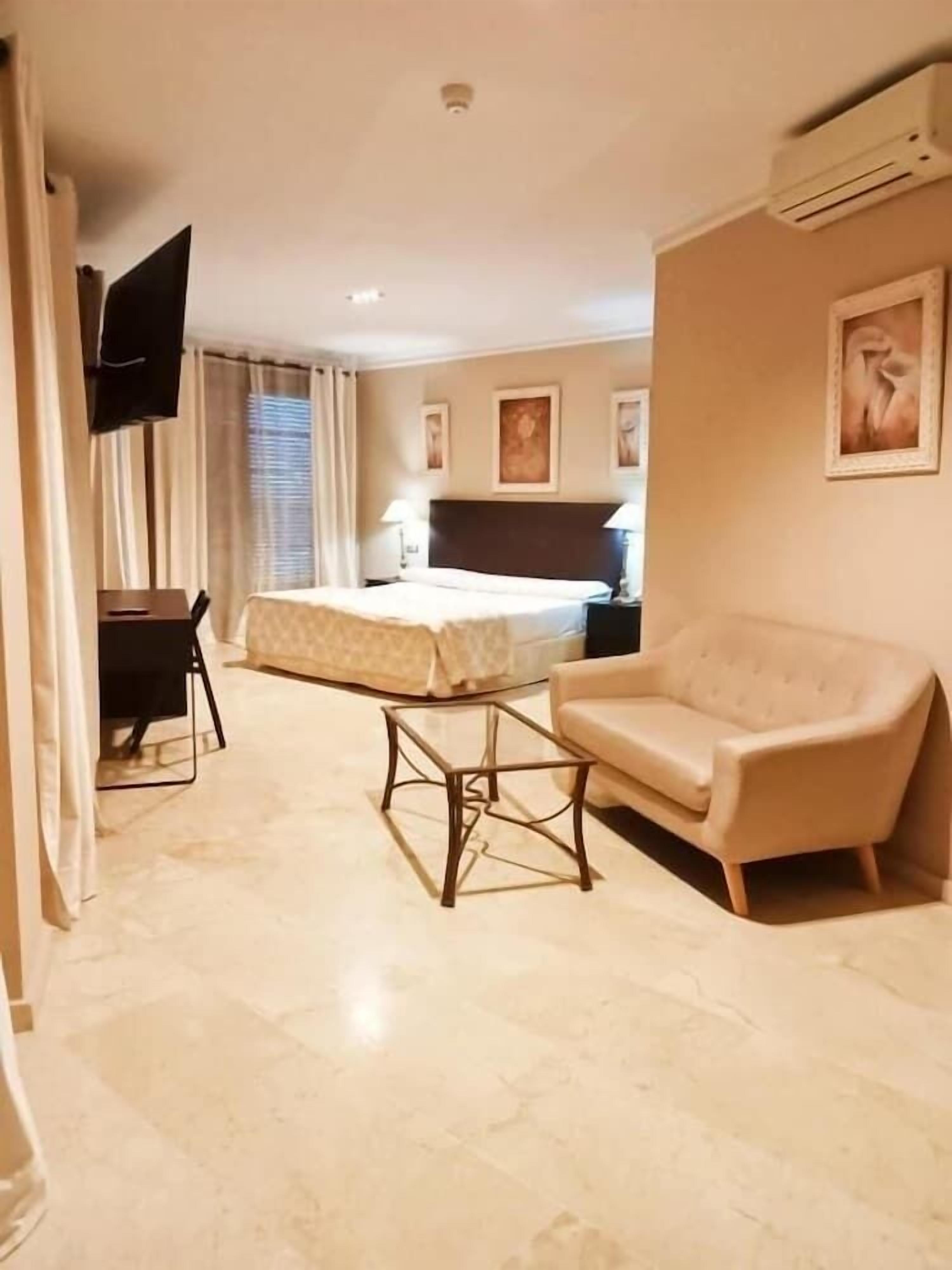 Una habitación de hotel con una cama, un sofá, una mesita, un televisor y un cuadro en la pared.